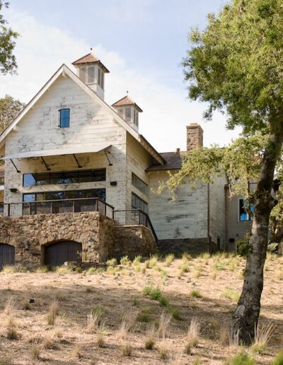 A large, rustic building in a woodland clearing, showing signs of weathering and disrepair.