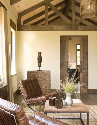 A cozy and rustic interior with a leather armchair, wooden furniture, and exposed ceiling beams.