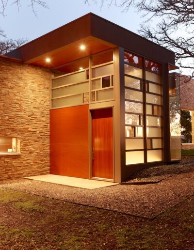 Modern entrance of a building with a large, open red door and glass facade during dusk.