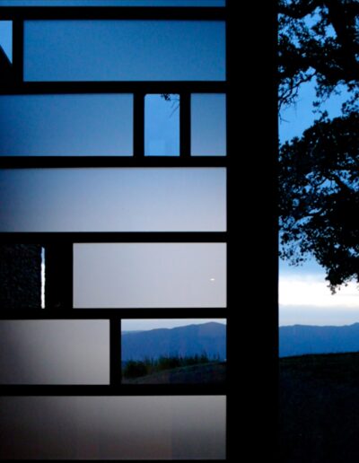 Twilight view through a window with multiple panes, showing silhouetted trees and distant mountains.