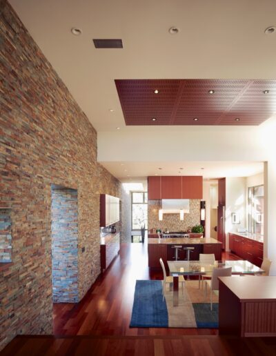 Modern interior with wooden floors, brick walls, and a view into a kitchen with a red accent ceiling.