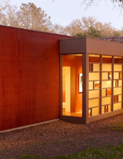 Modern red building with large windows illuminated from within at dusk.
