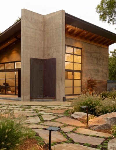 Modern house with large pivoting front door and landscaped garden at dusk.