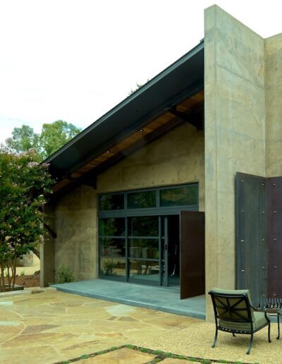 Modern house with a distinctive concrete tower feature, large windows, and a landscaped garden with a seating area.