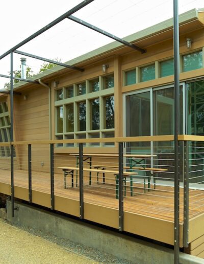 Modern building featuring a metallic frame with large windows and a wooden exterior, complete with an accessible ramp and an outdoor seating area.