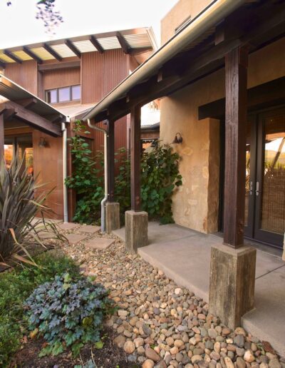 Rustic styled pathway with decorative pebbles leading to a building with wooden beams and green climbing plants.