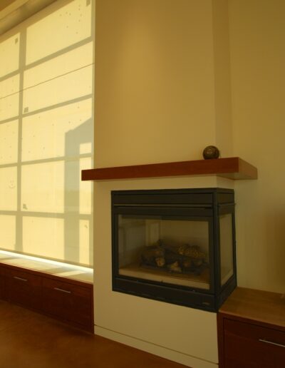 A modern hearth with a floating wooden mantel and a built-in fireplace, flanked by clean-lined cabinetry and a large window with minimalistic blinds.