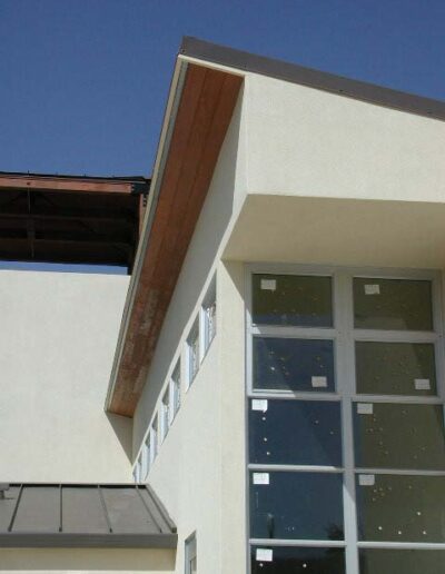 Modern building corner with protruding roof and large windows.