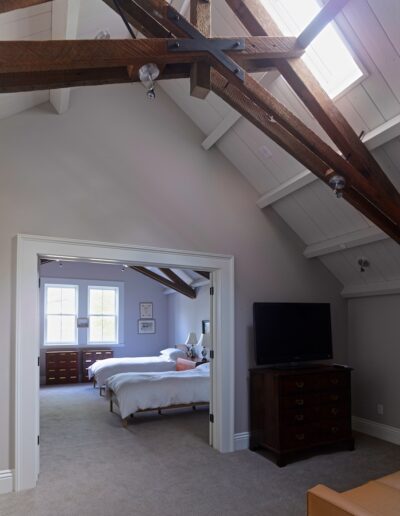 An airy bedroom with exposed wooden beams, skylights, and a vaulted ceiling.