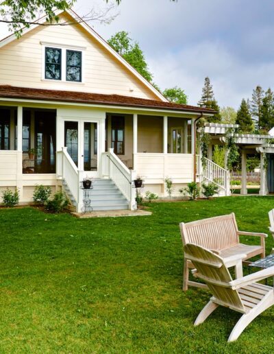 Classic country house with a porch and lawn chairs, adjacent to a large greenhouse.