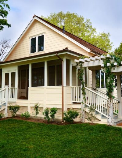 Charming single-story home with white trim and a pergola over a path in a green lawn setting.