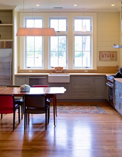A modern kitchen with wooden floors, gray cabinetry, stainless steel appliances, and a dining area with a red table and chairs.