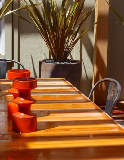 Sunny patio setting with a glossy wooden table and red candle holders, next to a potted plant.